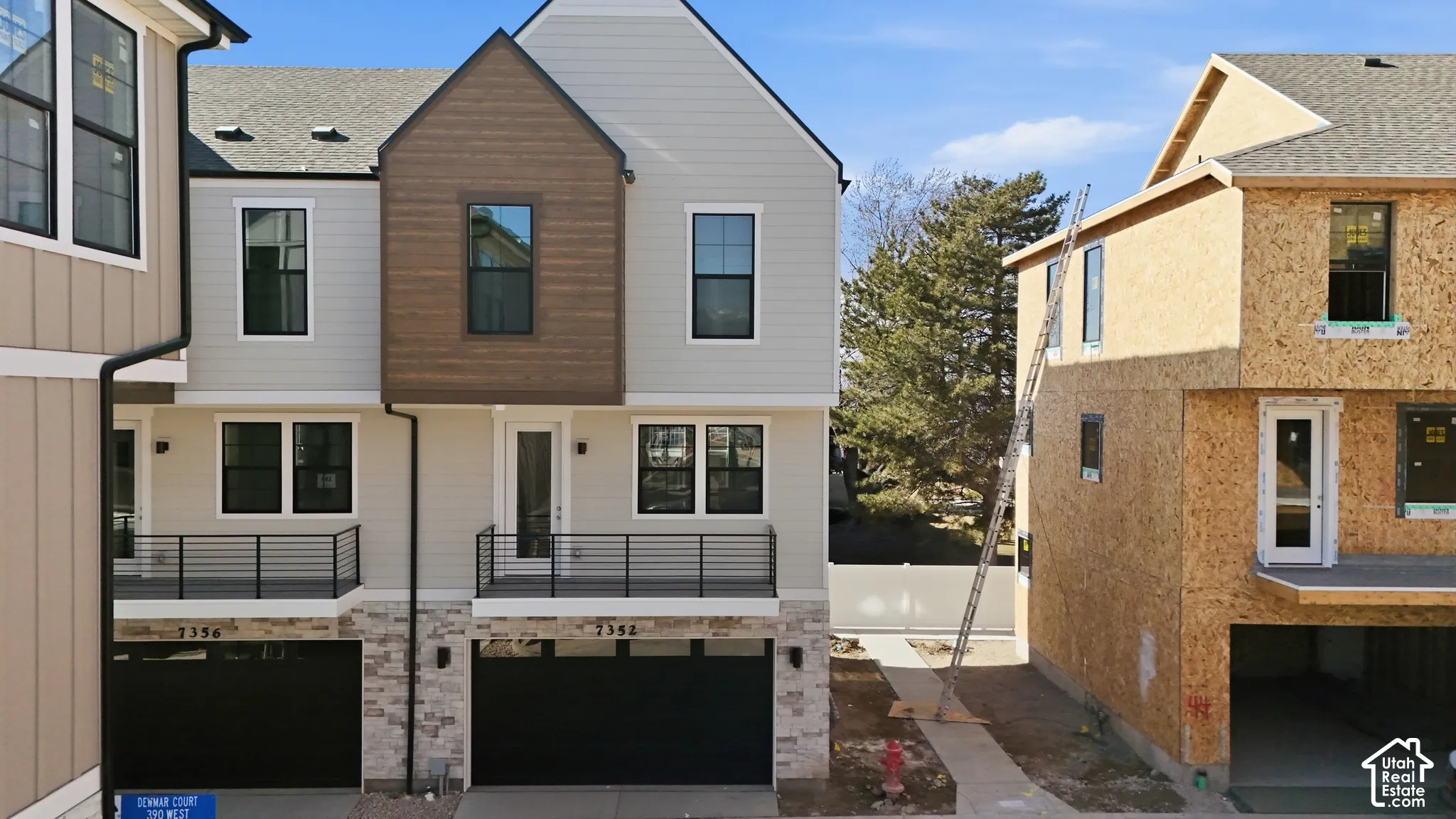 Multi-story exterior featuring horizontal lap siding, wood-finish accents, stone veneer foundation, black metal railing balconies, and two-car garage doors