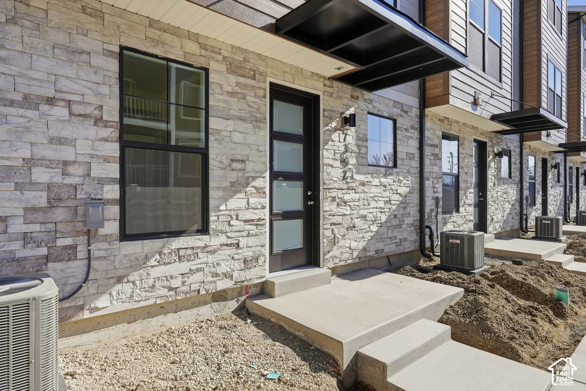 Modern townhouse exterior featuring a stacked stone veneer facade, dark-framed windows, a multi-pane entry door with frosted glass insets, and a black metal awning