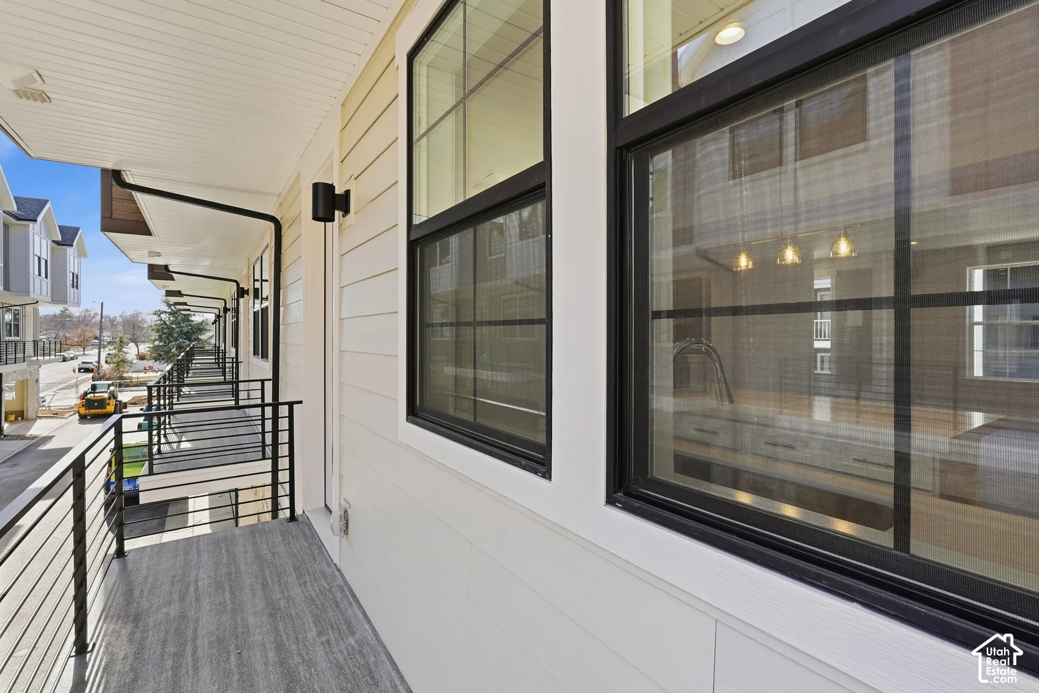 Exterior balcony featuring wood-finish flooring, horizontal siding, metal railing with cable infill, and black-framed windows