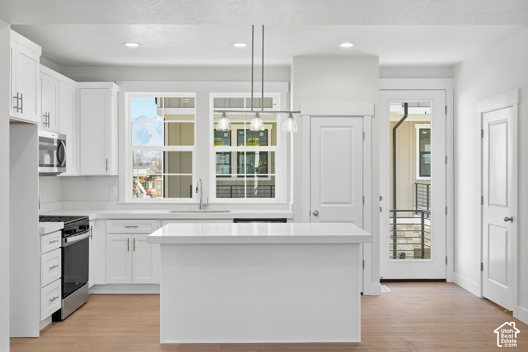 Kitchen featuring white cabinetry, an island with a solid surface countertop, wood-finish flooring, stainless steel appliances, and mountain scenery