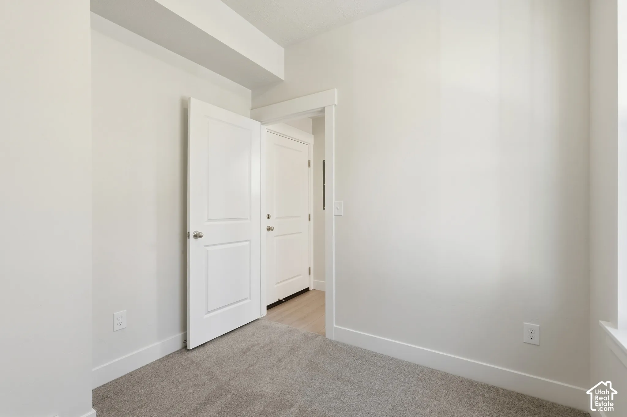Neutral-toned interior space featuring wall-to-wall carpeting, crisp white walls, and two-panel interior doors