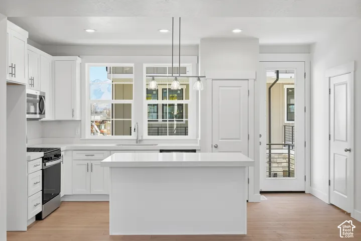 Kitchen featuring white cabinetry, an island with a solid surface countertop, wood-finish flooring, stainless steel appliances, and mountain scenery