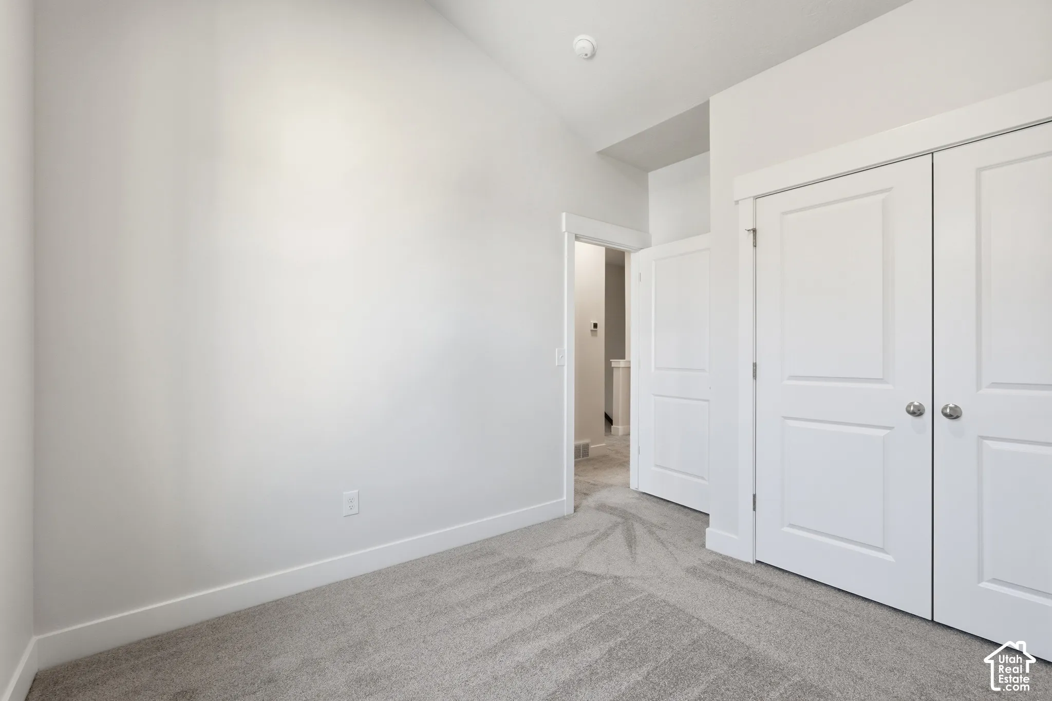 Vaulted ceiling, neutral wall tones, plush wall-to-wall carpeting, and double-panel closet doors with brushed nickel hardware