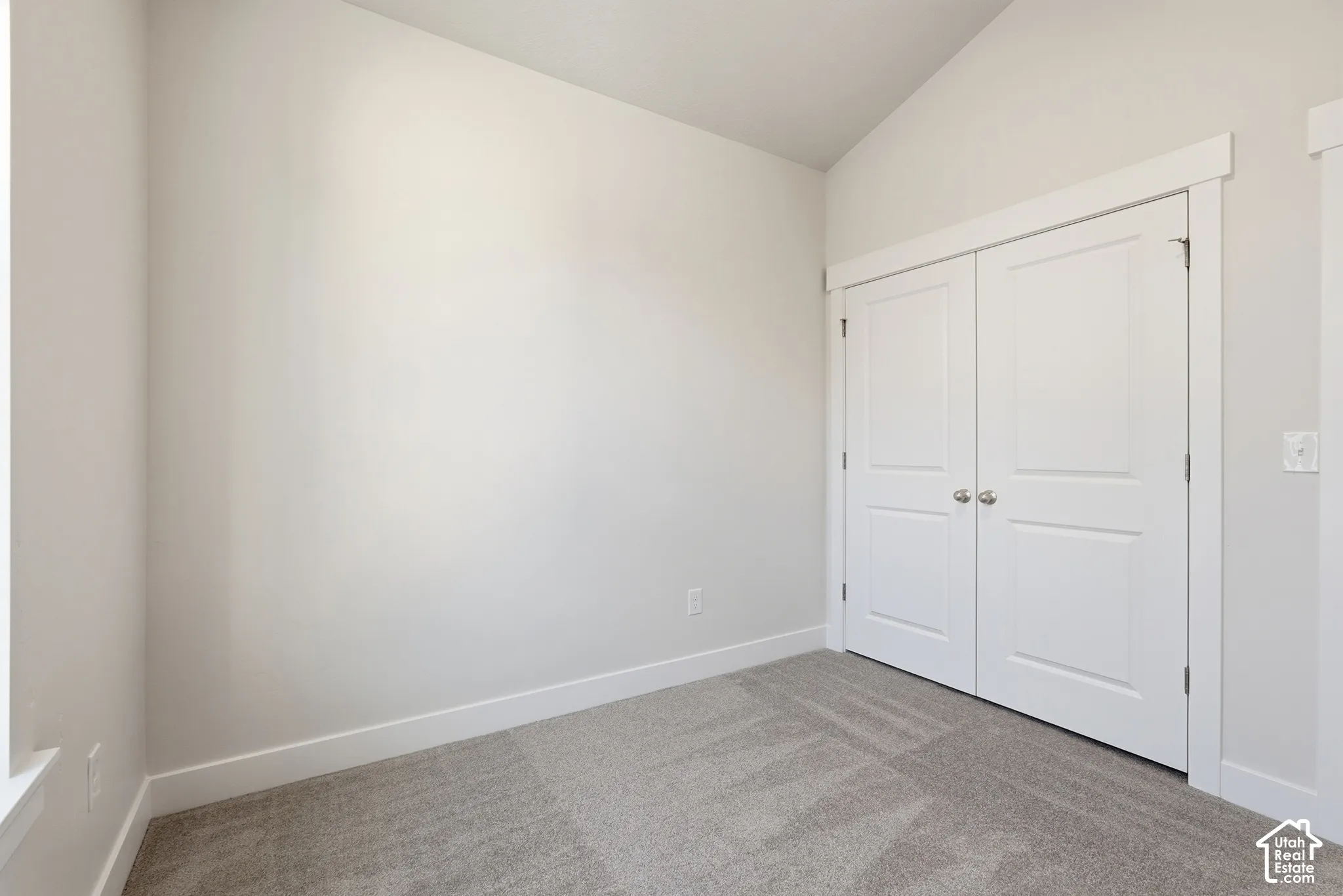 Vaulted ceiling featuring neutral wall paint, carpeting, and double-panel doors with white trim