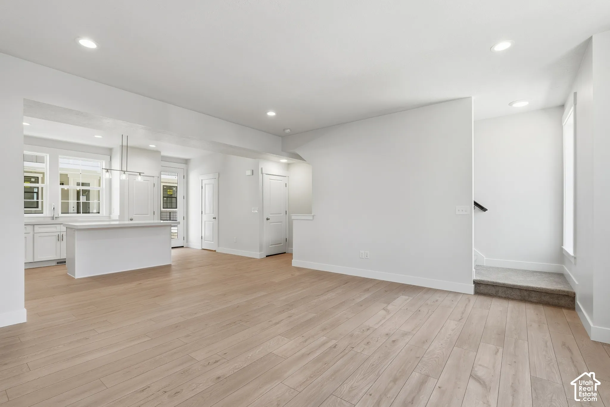 Open concept interior featuring wood-finish flooring, recessed lighting, white kitchen cabinetry with a central island, and a tiered staircase