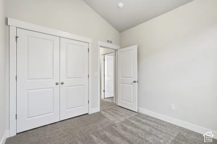 Room featuring a vaulted ceiling, neutral wall tones, carpeted flooring, two-panel interior doors, and door casing trim
