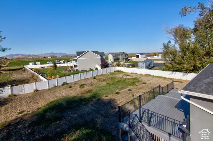 Elevated composite deck with black metal railing, expansive yard space, full-perimeter white vinyl fencing, and mountain scenery
