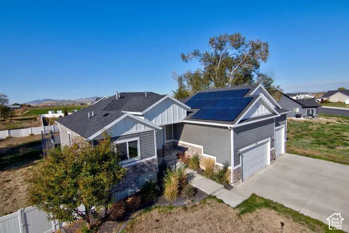 Exterior featuring horizontal siding, stone veneer accents, an asphalt shingle roof with integrated solar panels, and a multi-car garage