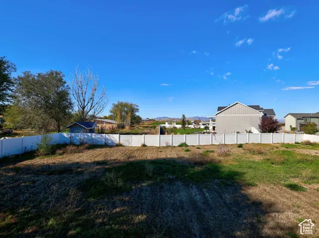 Expansive backyard featuring a white vinyl perimeter fence, mature trees, and mountainous horizon