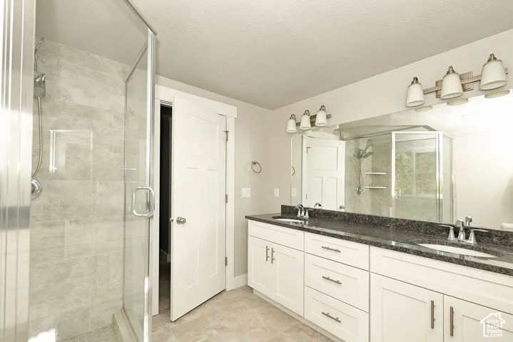 Dual-sink vanity with dark stone-finish countertop, white Shaker-style cabinetry, glass-enclosed shower with tiled surround, and large wall-mounted mirror