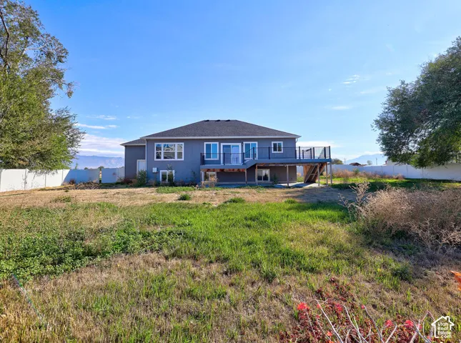 Rear exterior featuring a raised wooden deck with metal railing, multiple windows, sliding glass door, and full perimeter fencing