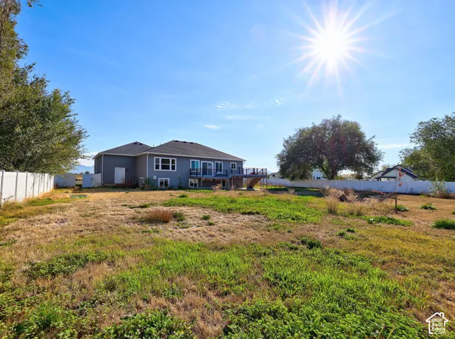 Expansive backyard featuring a raised wooden deck with metal railing, enclosed by full-perimeter white vinyl fencing