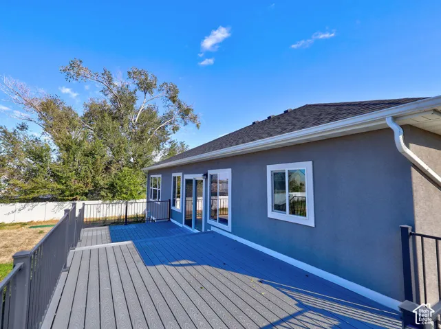 Elevated deck with composite wood-finish decking and dark metal railings, exterior stucco siding, sliding glass door, and vinyl-framed windows