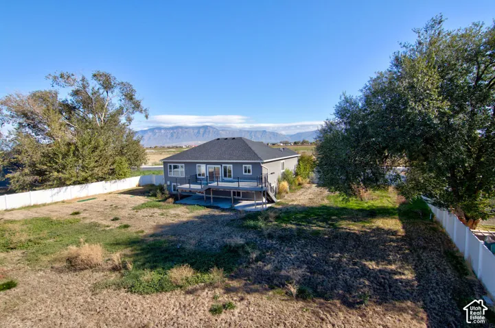 Rear exterior featuring a raised deck with metal railings, a paved patio, a vinyl privacy fence, and mountain scenery