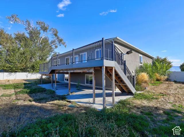 Elevated deck with metal railing, concrete patio, and exterior staircase