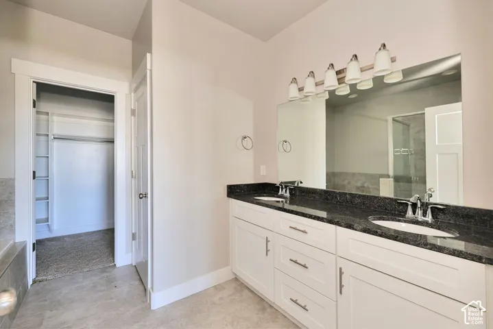 Dual-sink vanity with stone-finish countertop, white cabinetry with metal hardware, wall-to-wall mirror, multi-light fixture, and built-in closet shelving