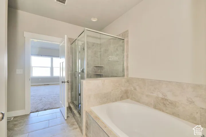 Oversized soaking tub with neutral stone-look tile surround, glass-enclosed shower with built-in shelving, and ceramic tile flooring