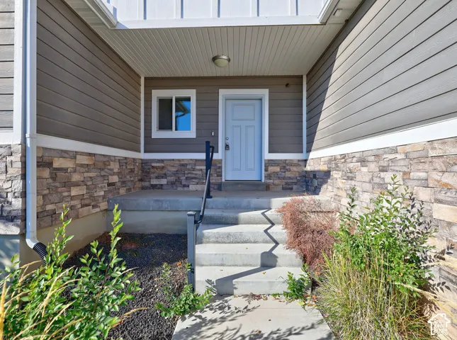 Covered entryway featuring horizontal lap siding, stone veneer accents, a solid-panel door, and a concrete staircase with a metal handrail