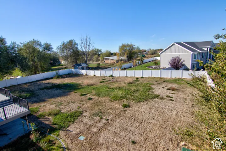 Expansive backyard featuring a white vinyl privacy fence, elevated deck with black railings, and open lot area