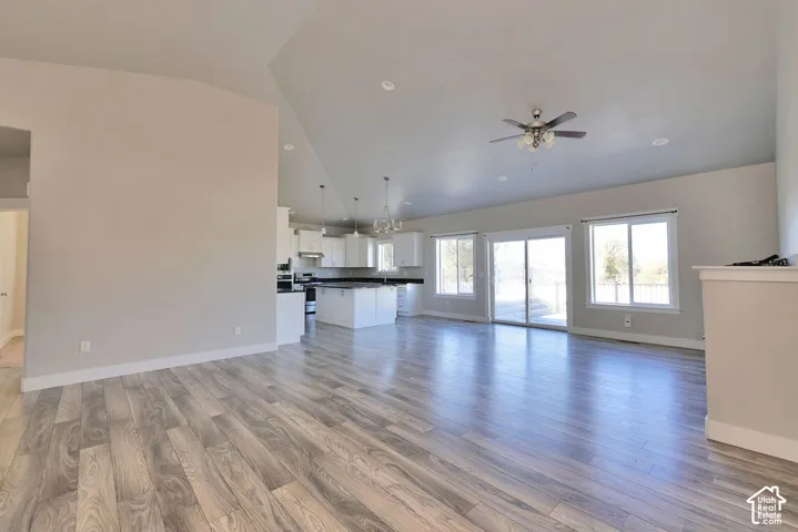 Vaulted ceilings featuring recessed lighting, wood-finish flooring, kitchen island with dark countertops, and sliding glass doors