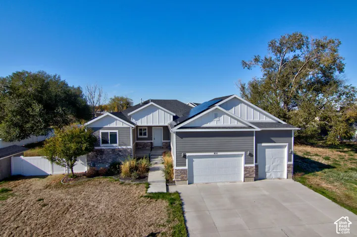 Multi-level exterior featuring a combination of horizontal siding and stone veneer, shingled roof with integrated solar panels, and a three-car garage