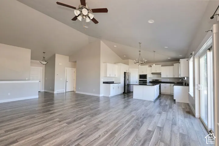 Vaulted ceilings, wood-finish flooring, kitchen island with dark countertops, white shaker-style cabinetry, and sliding glass doors