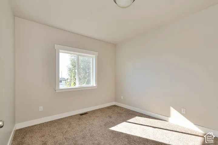 Neutral-toned walls, plush wall-to-wall carpeting, window with wide-profile white casing, and a flush-mount ceiling fixture