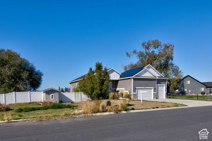Single-story residence featuring horizontal siding, stone veneer accents, roof-mounted solar panels, a concrete driveway, and a white vinyl privacy fence