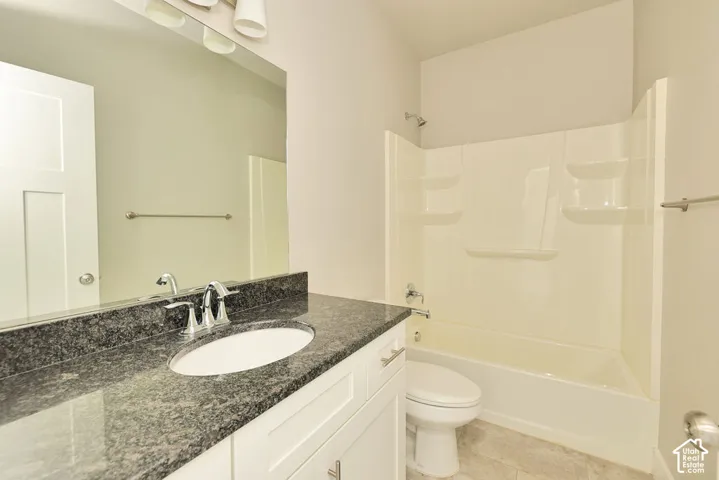 Full-width vanity with stone countertop, integrated sink, white shaker-style cabinetry, large wall-mounted mirror, and a tub-shower combination with integrated shelving