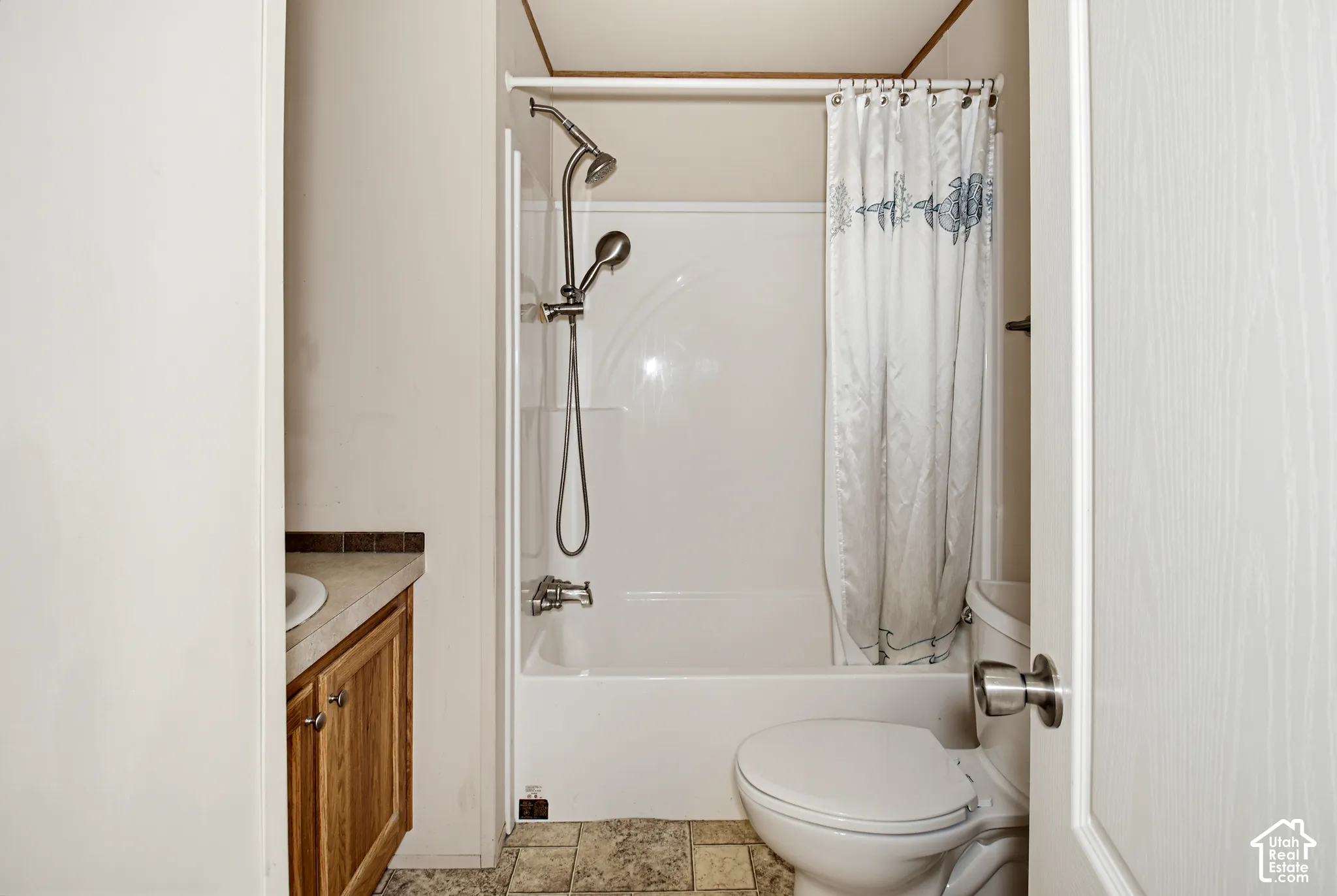 Bathroom featuring a white tub-and-shower combination, multi-function handheld showerhead, wood-finish vanity cabinet, solid-surface countertop with integrated sink, and tile-finish flooring