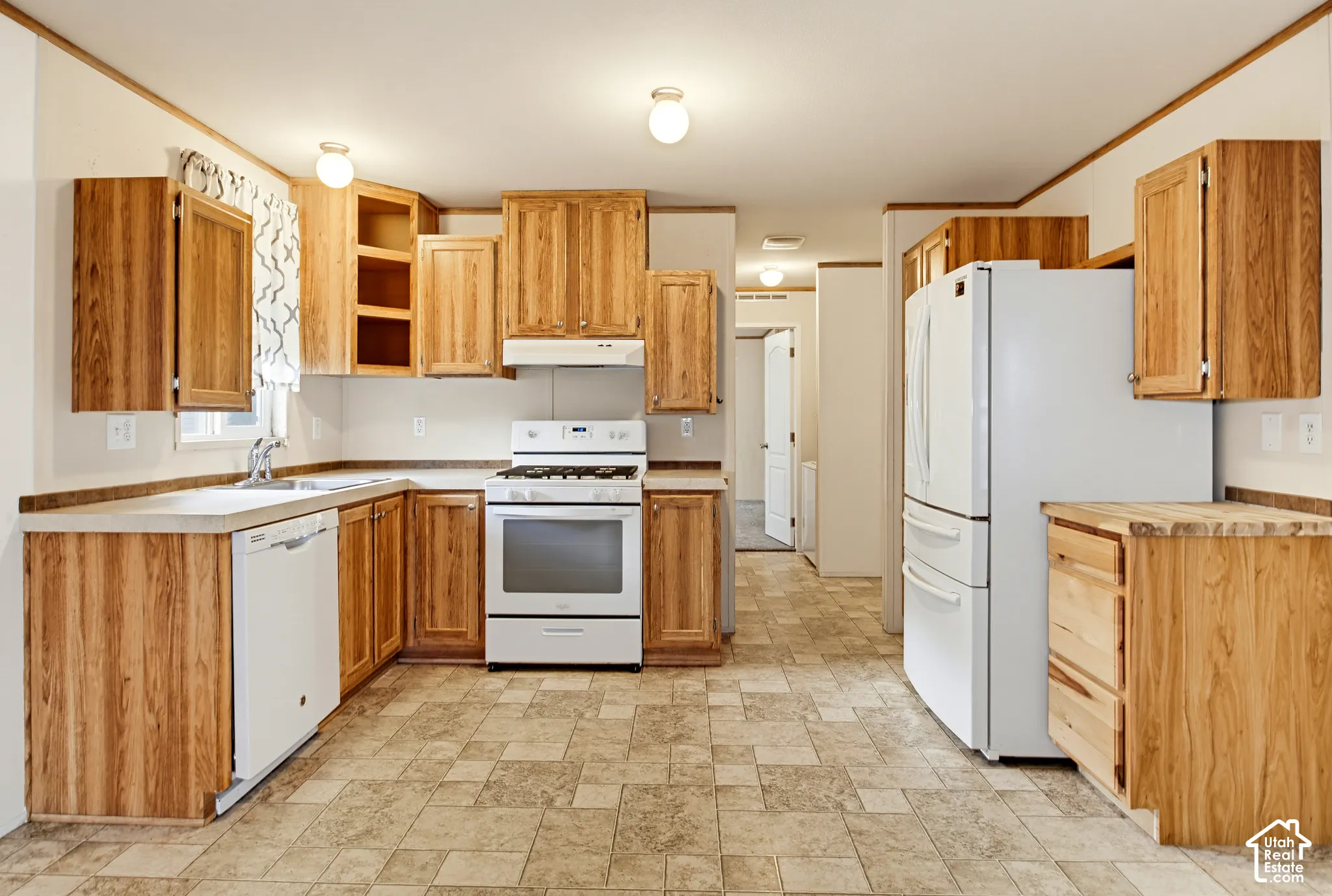 Kitchen featuring natural wood-finish cabinetry, solid-surface countertops, tile-patterned flooring, and white kitchen appliances