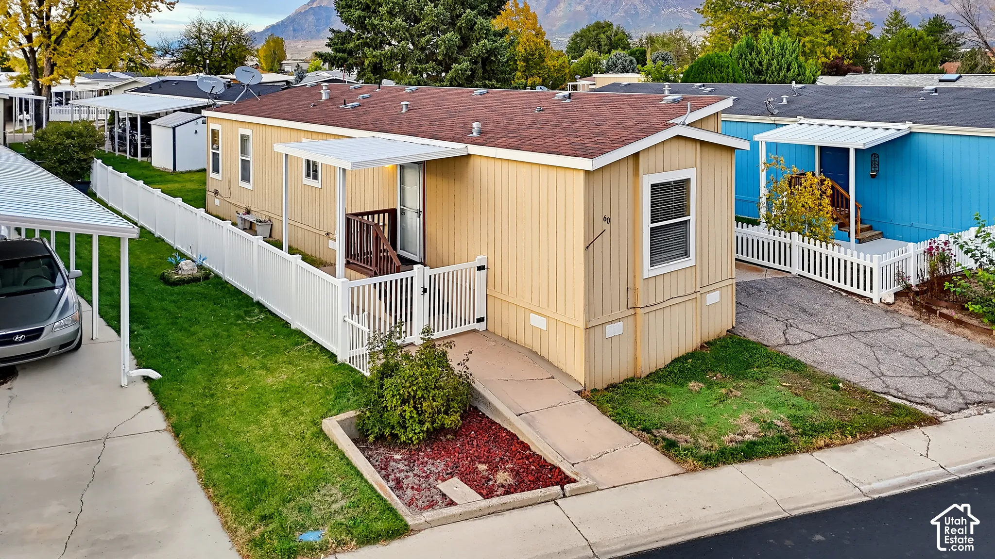Exterior featuring a beige panelled facade, asphalt shingle roof, covered entryway, gated vinyl fencing, and dedicated carport