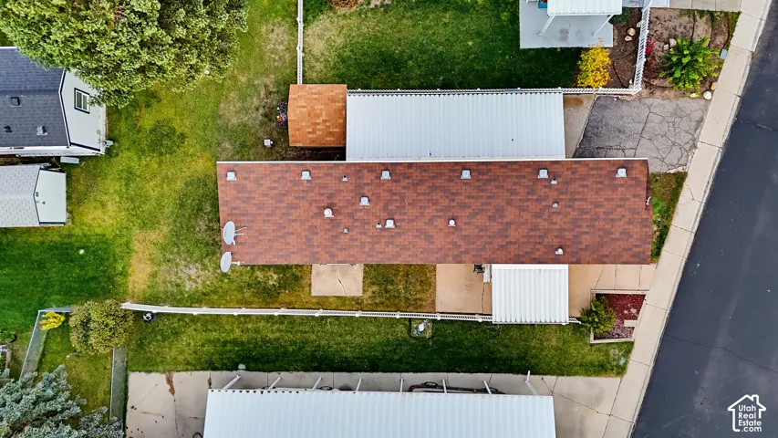 Aerial view of property featuring a shingled roof, dual covered parking structures, concrete patio, and fenced outdoor space