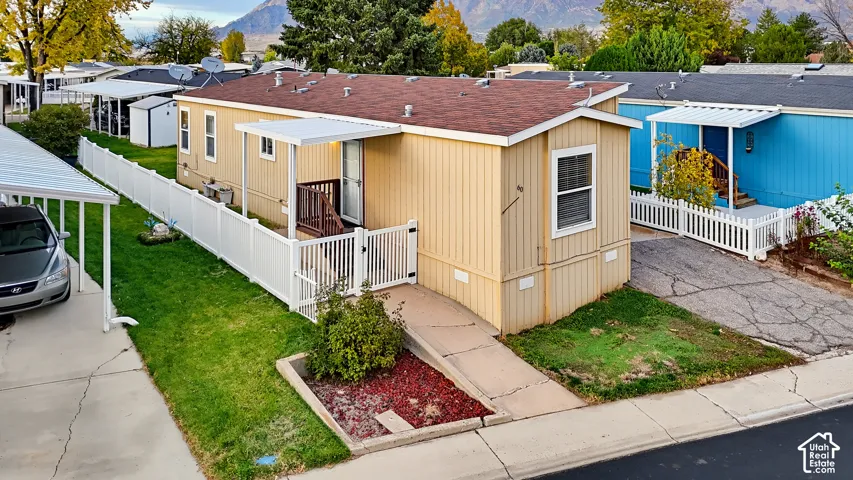 Exterior featuring a beige panelled facade, asphalt shingle roof, covered entryway, gated vinyl fencing, and dedicated carport