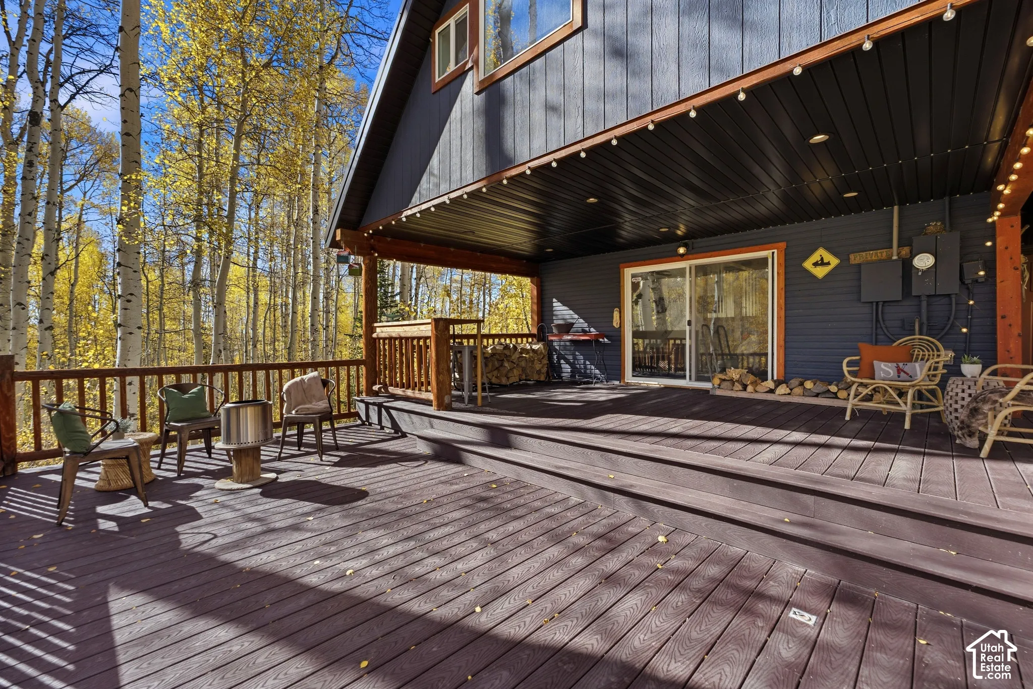 Expansive multi-level wood deck featuring built-in wood railing, recessed soffit lighting, and natural backdrop of mature aspen trees
