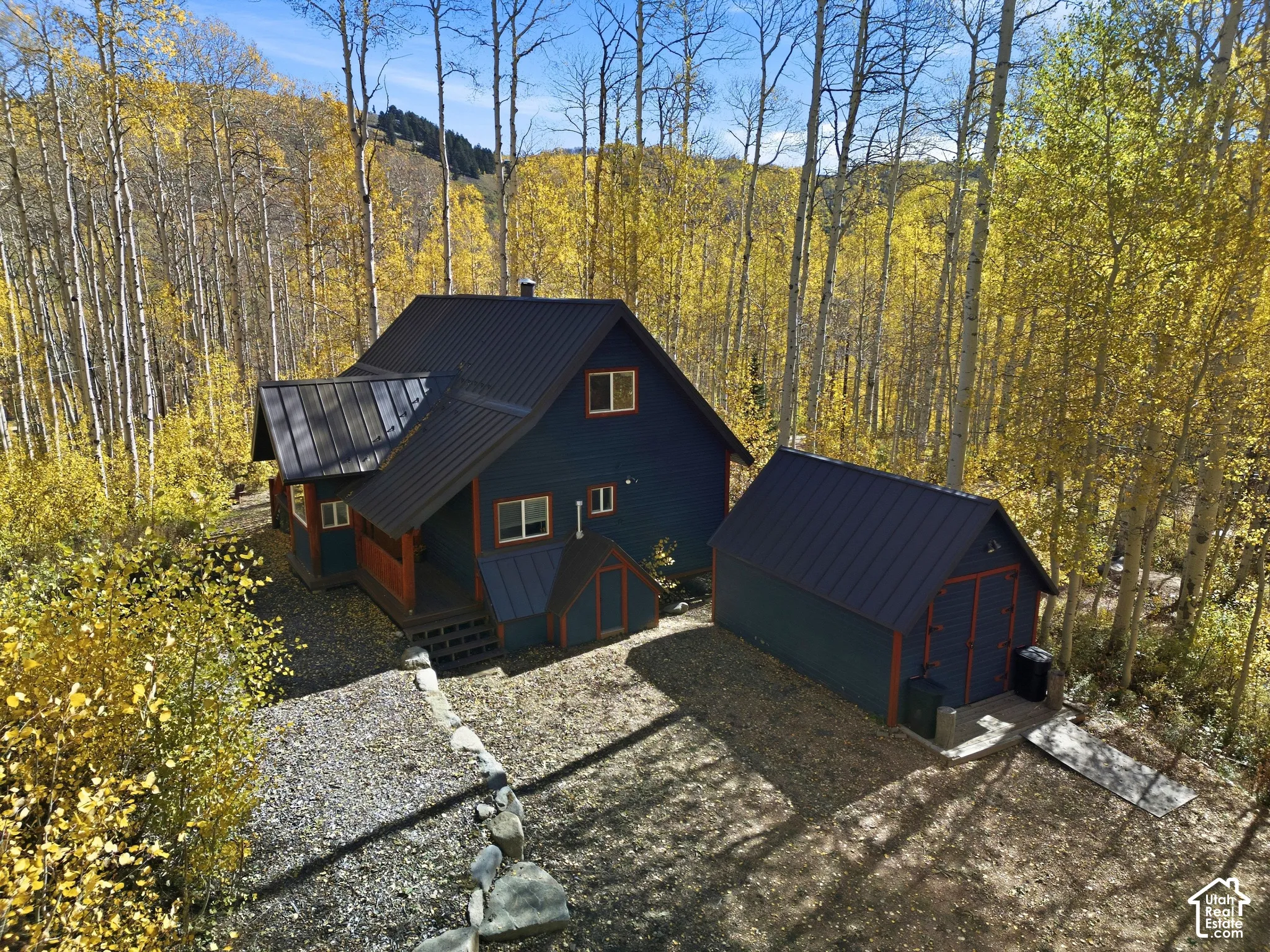 Multi-level exterior featuring dark-toned siding with contrasting trim, a metal roof, an attached outbuilding, and stone hardscaping
