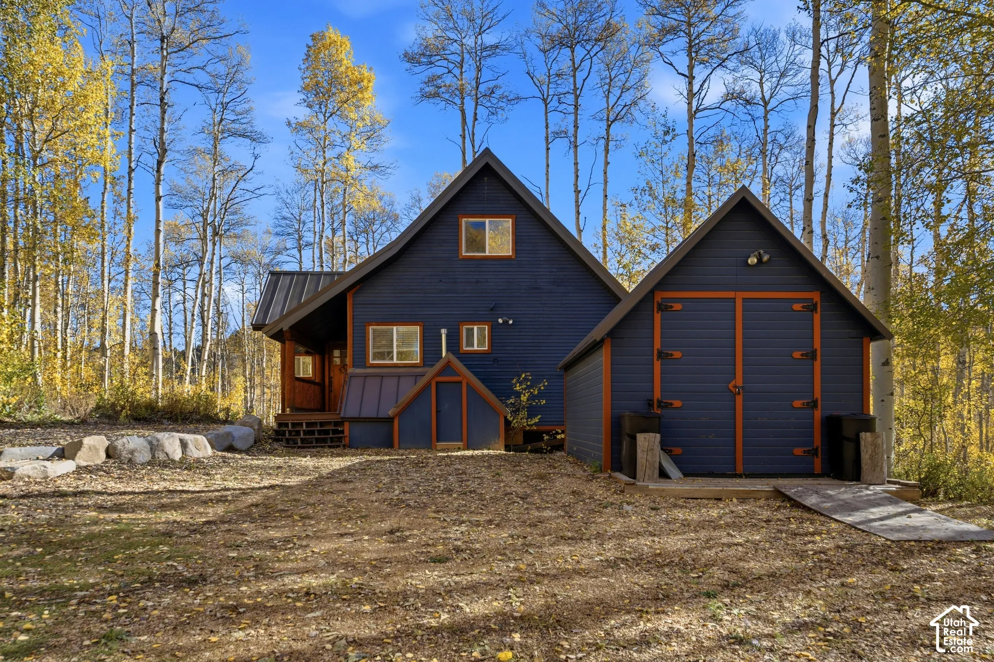 Two-story exterior featuring painted wood siding with contrasting trim, a metal roof, and an attached garage structure situated on a wooded lot with natural stone landscaping