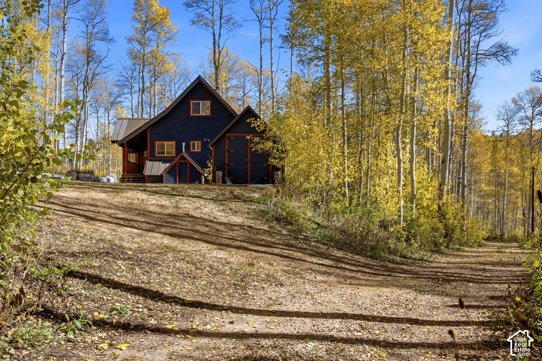 Dark-hued siding with wood trim, multiple gabled rooflines, standing seam metal roofing, and natural woodland surroundings
