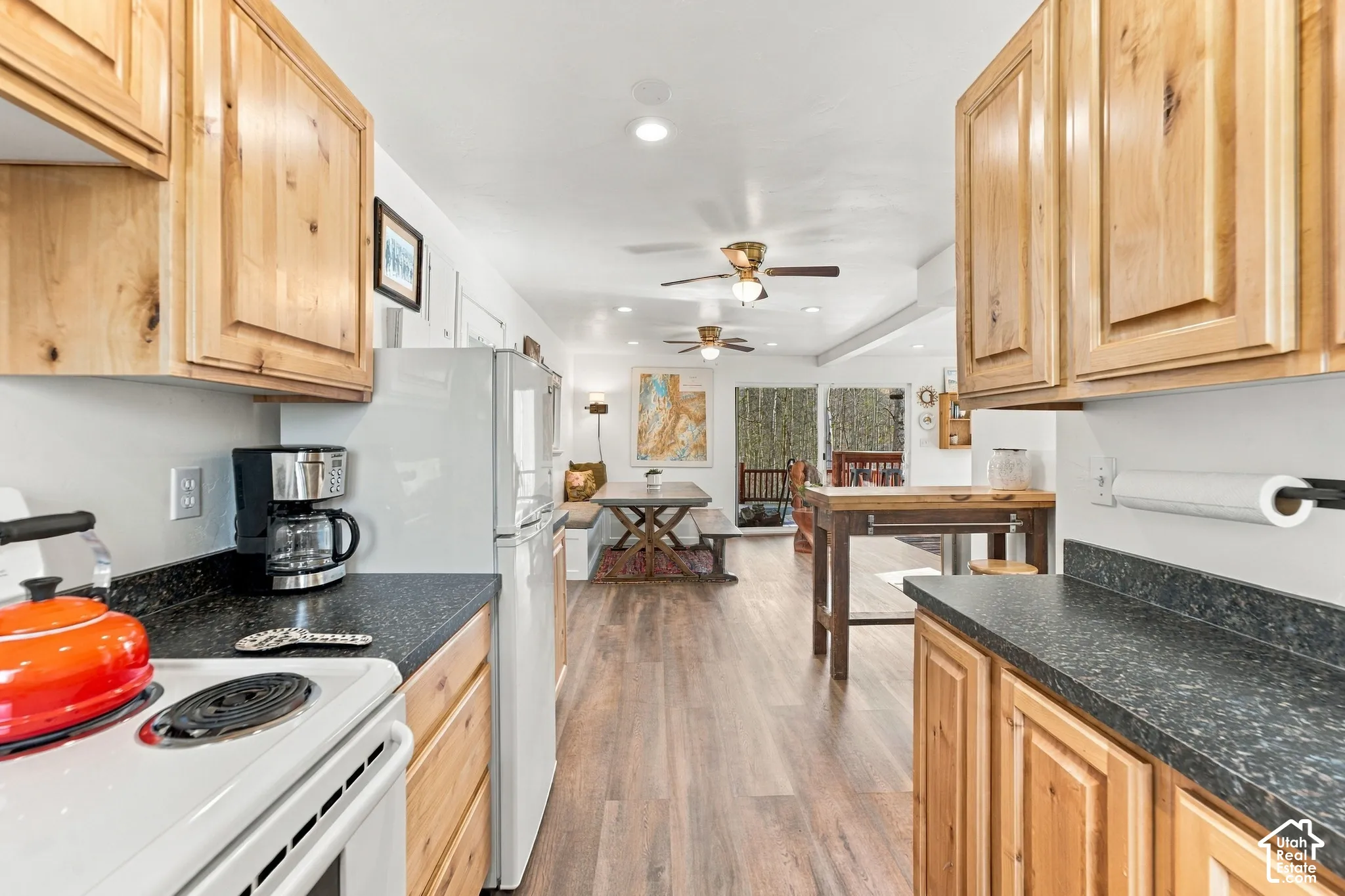 Kitchen featuring natural wood-finish cabinetry, dark solid-surface countertops, wood-finish flooring, and dual ceiling fans