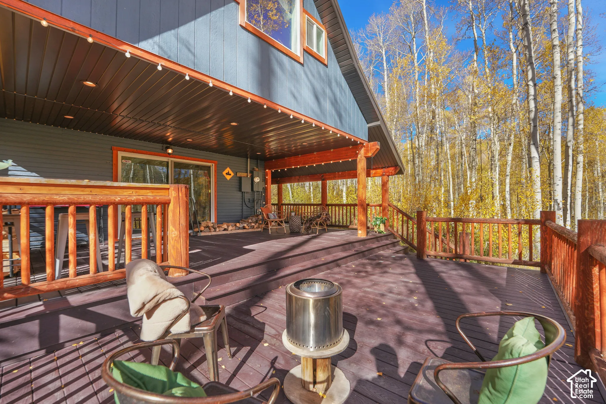 Expansive wood-decked patio featuring a covered area with recessed lighting, timber support beams, and a natural woodland backdrop