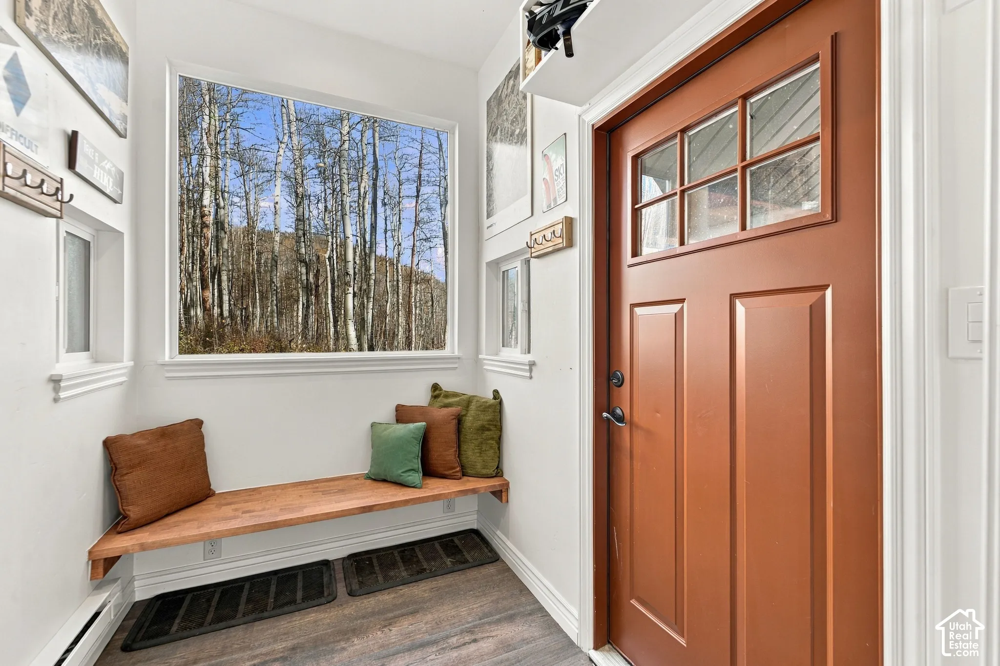 Entryway featuring a solid door with a multi-pane glass insert, wood-finish flooring, a built-in floating bench, and a large picture window showcasing forest scenery