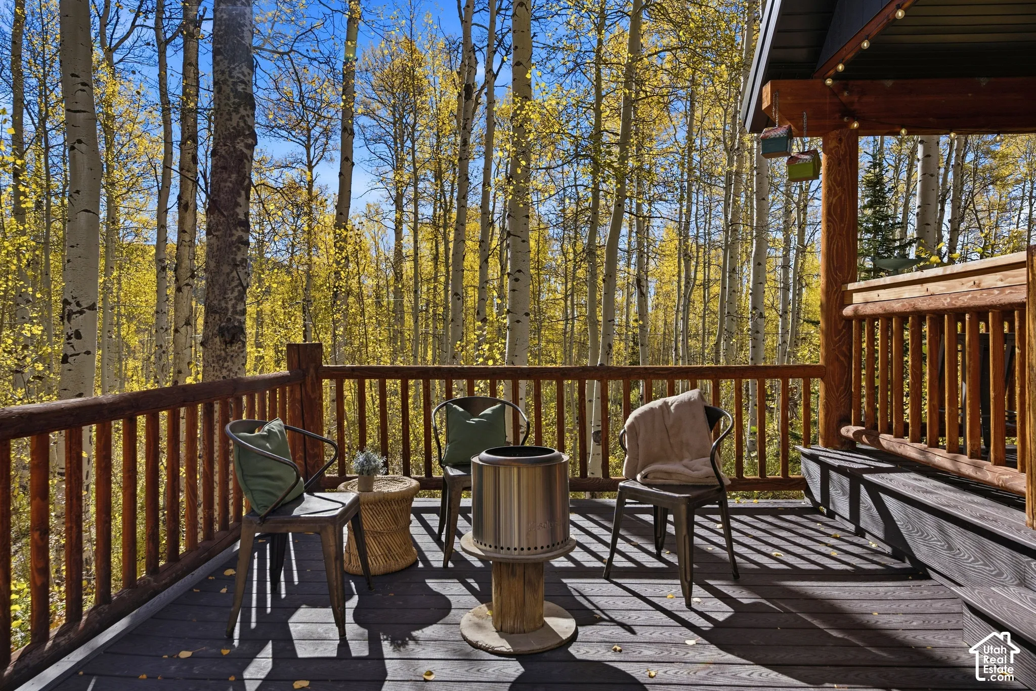 Covered wood deck featuring timber log railings and composite decking, surrounded by mature aspen trees