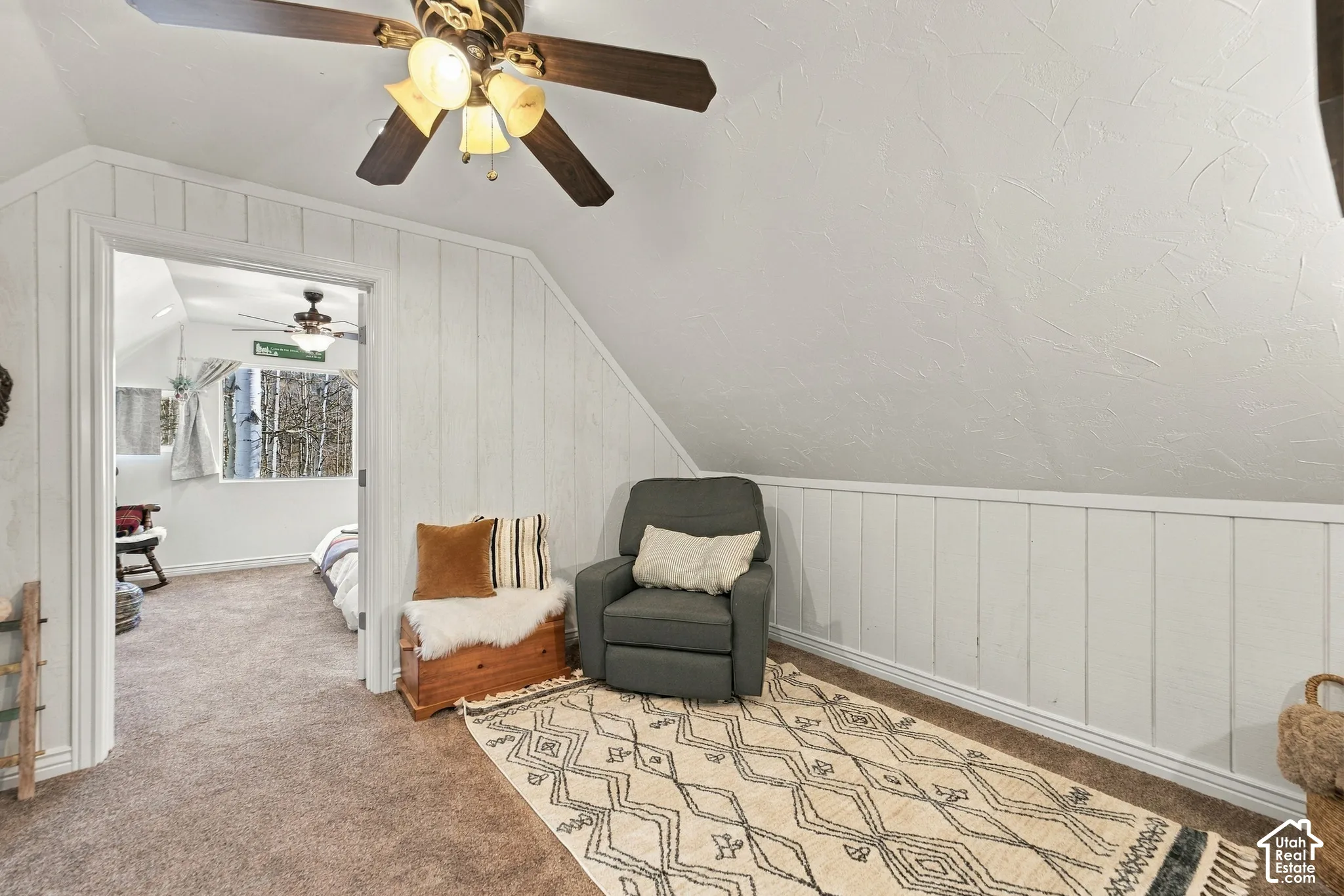 Room featuring white vertical wood paneling, textured wall finishes, carpeted flooring, and a ceiling fan with integrated lighting