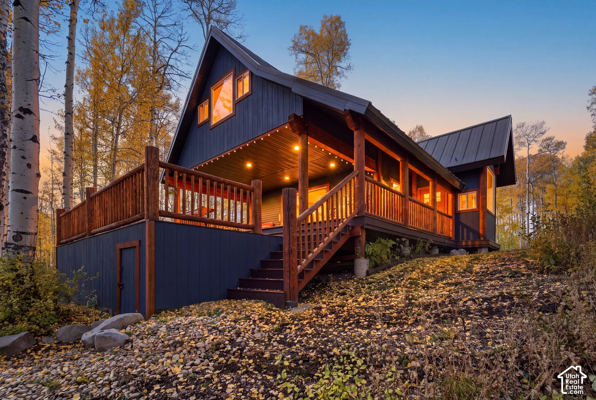 A-frame structure featuring dark vertical siding, a metal roof, an expansive wood-railed deck, and exposed timber structural elements