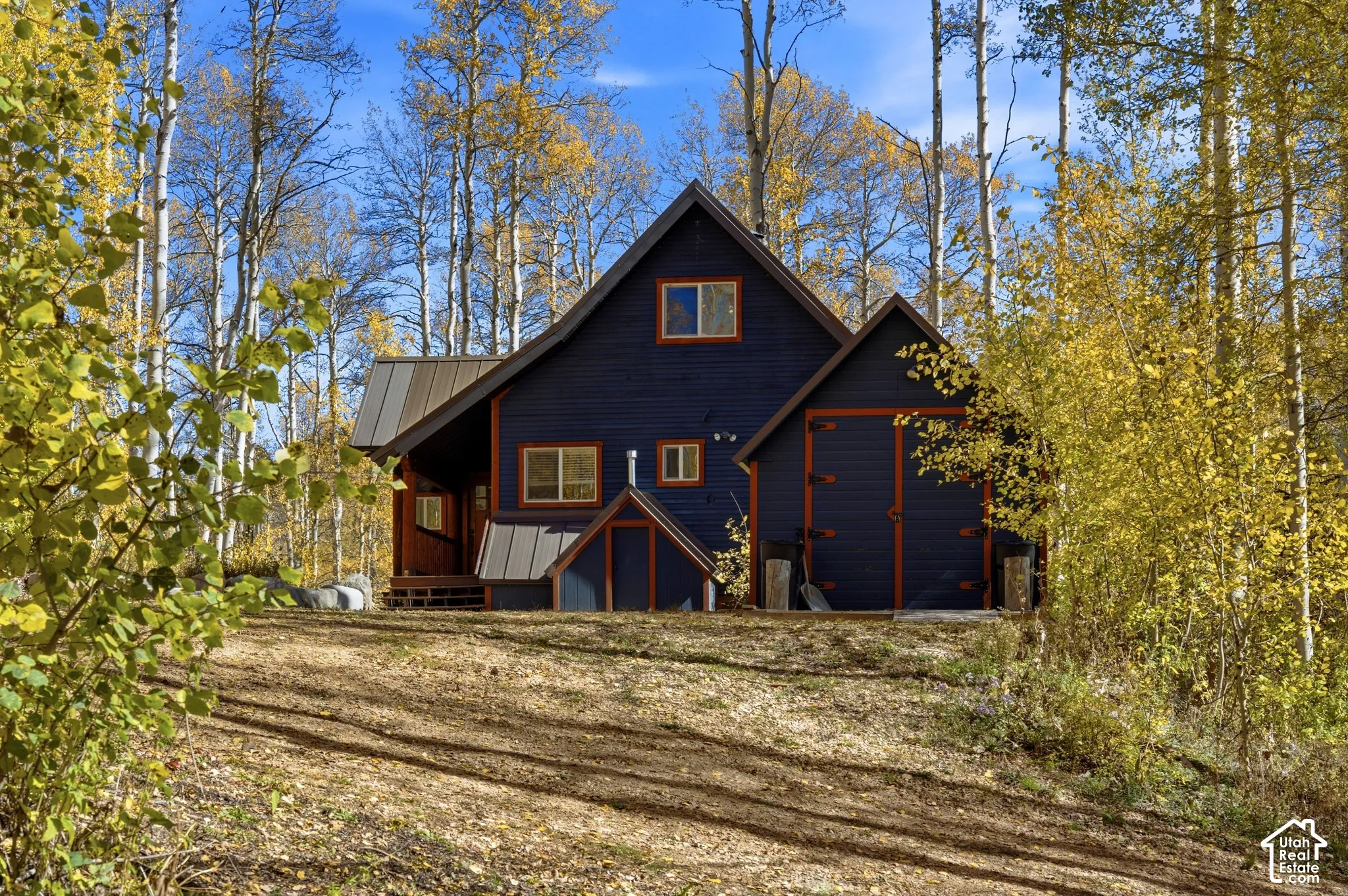 Dark-stained wood siding with contrasting trim, metal roofing, integrated garage, and natural woodland surroundings