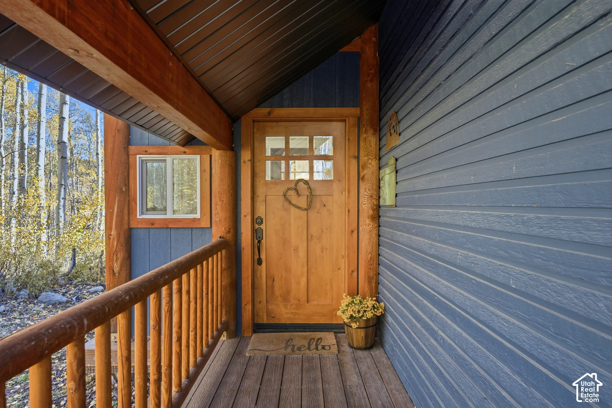 Covered entry porch featuring natural wood log railings, horizontal lap siding, and a solid wood door with a multi-pane glass window