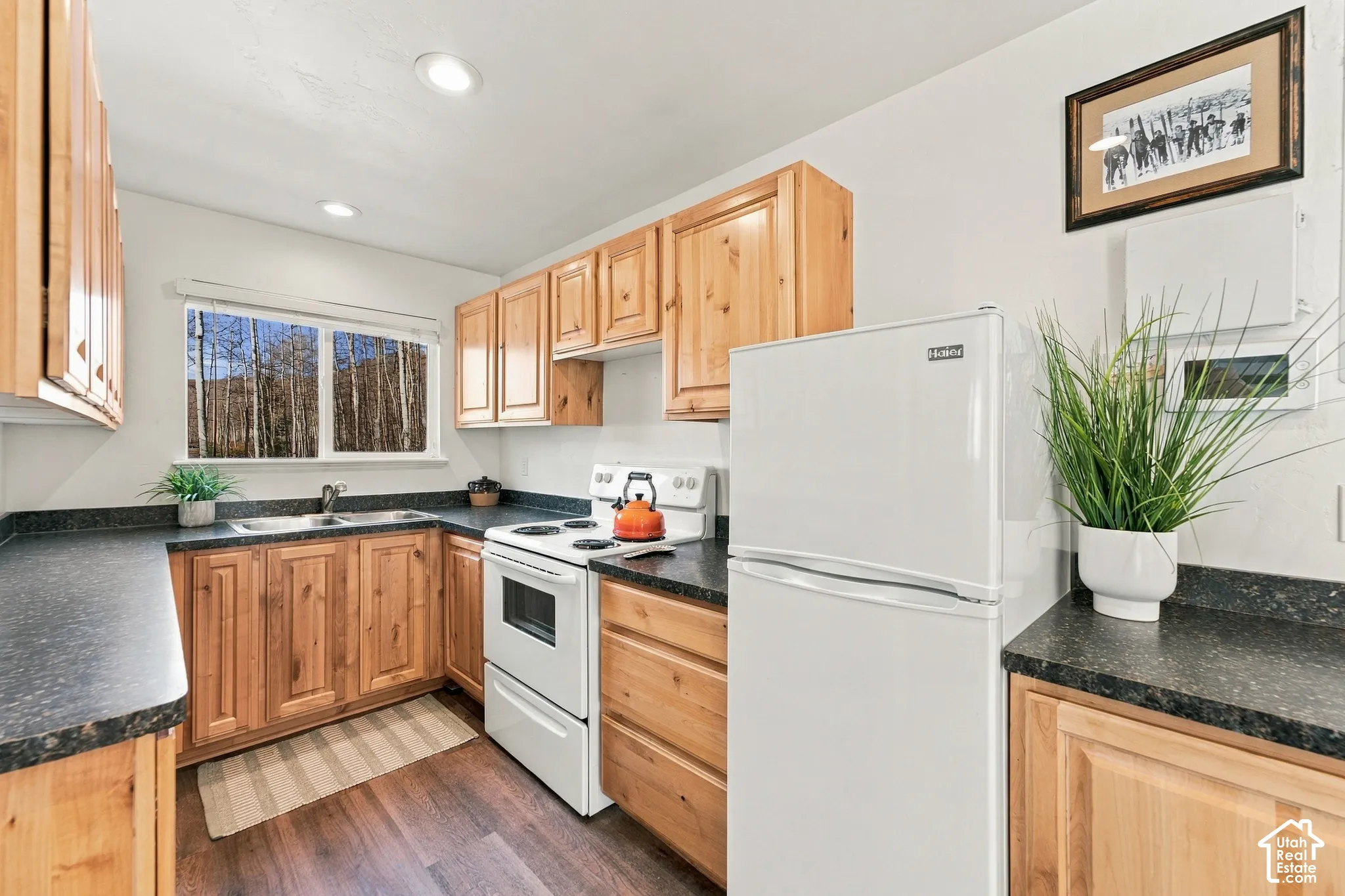 Kitchen featuring natural wood-finish cabinetry, dark countertops, white appliances, and wood-finish flooring