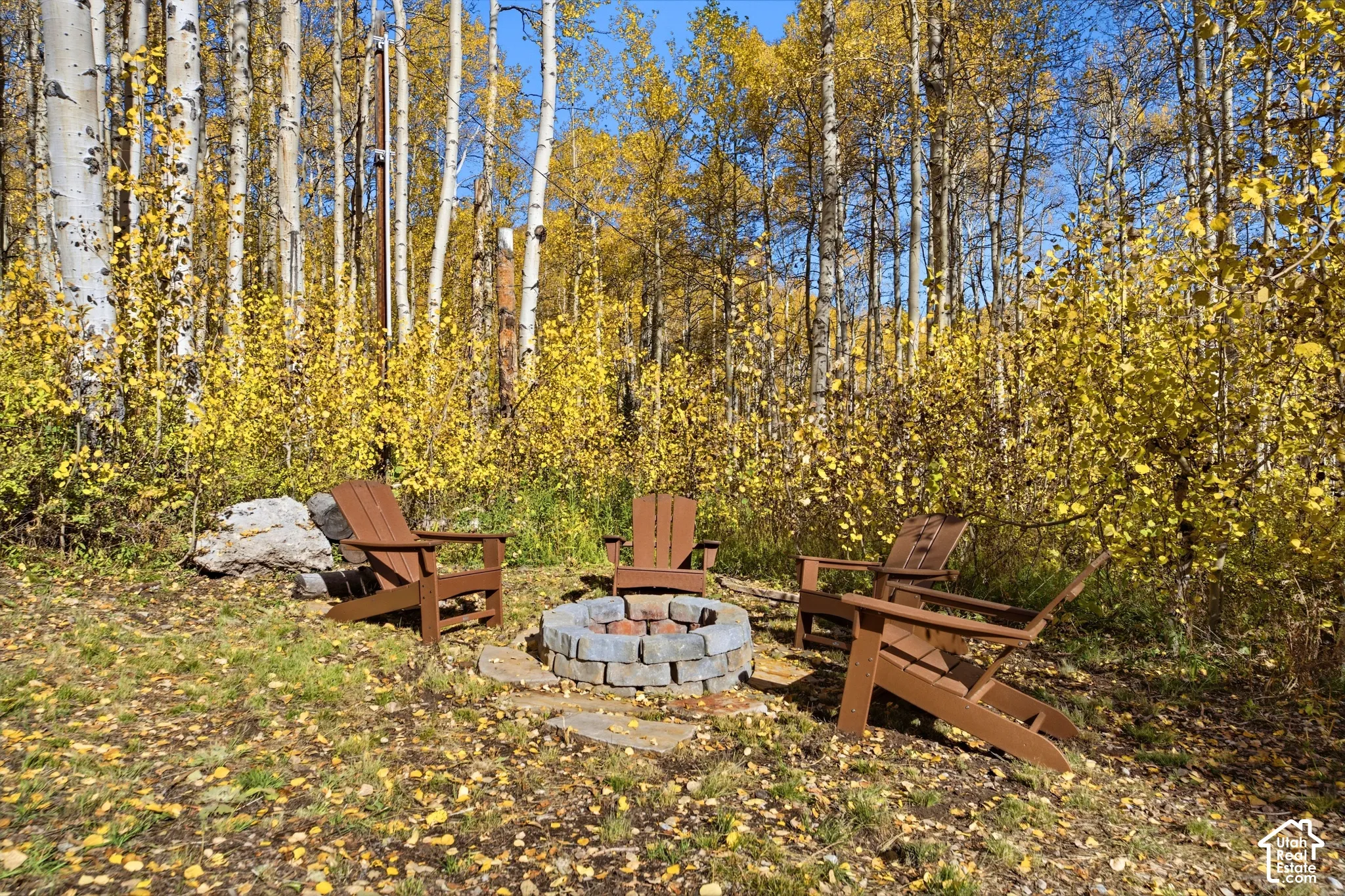 Outdoor fire pit constructed of stacked masonry blocks, situated within a wooded grove of aspen trees