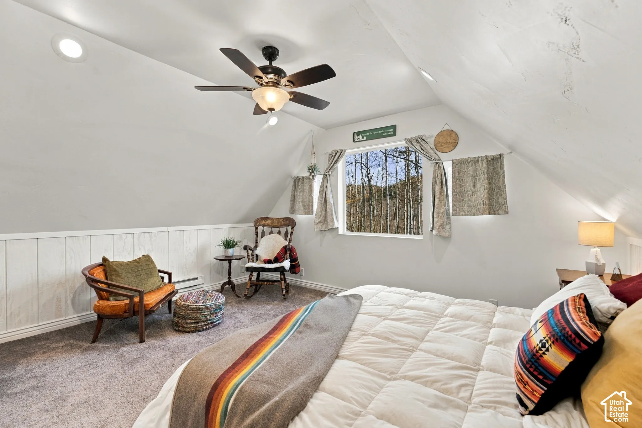 Vaulted ceiling room featuring paneled wall detailing, recessed lighting, a ceiling fan with integrated light fixture, and a window with exterior forest scenery