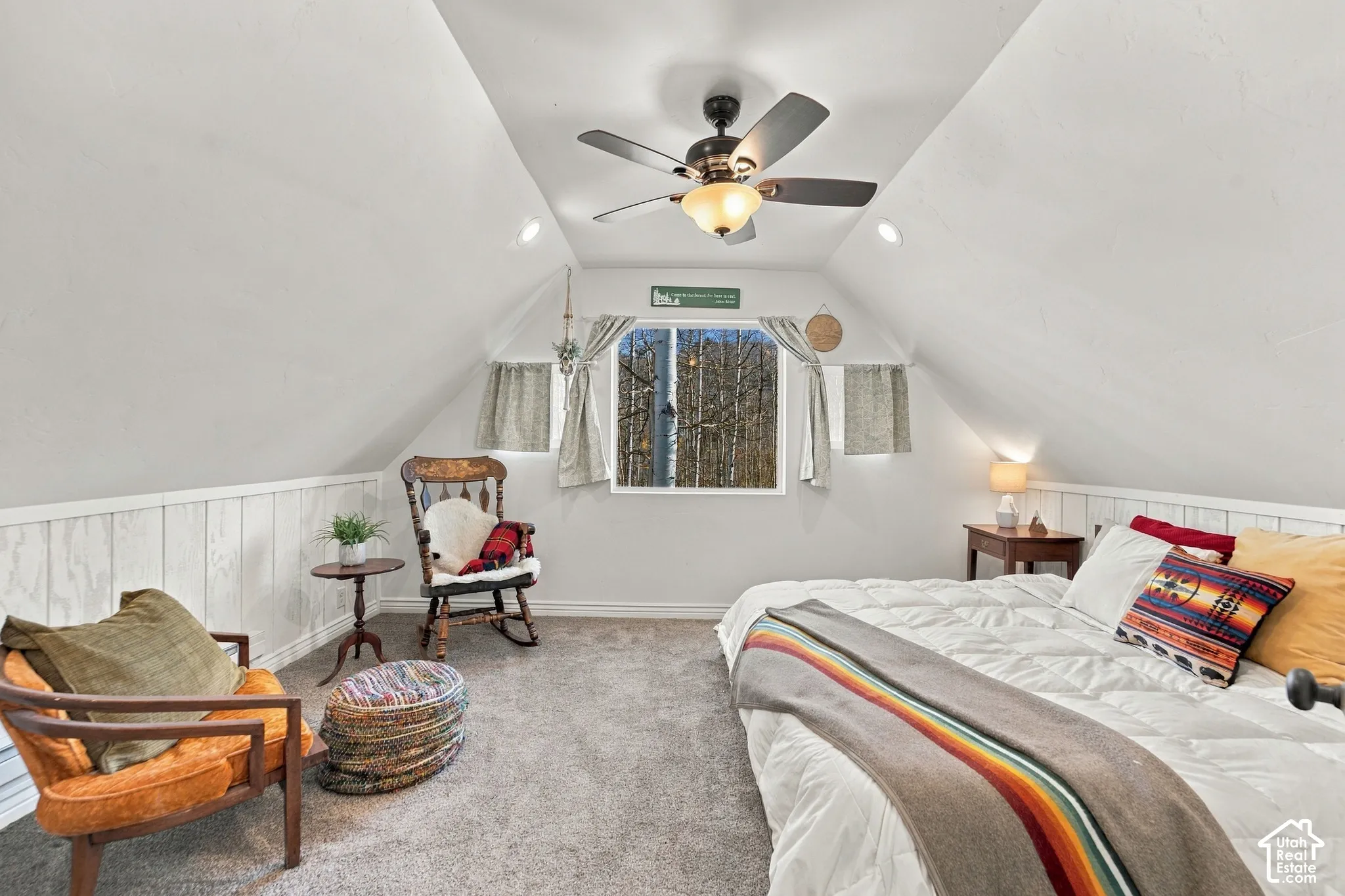 Vaulted ceiling with a central multi-blade ceiling fan, light-toned wall paneling, and a dual-pane window